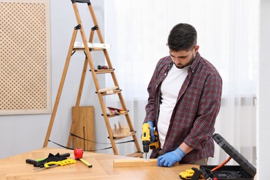 Young handyman working with electric drill at table in workshop