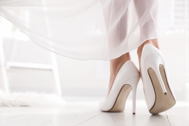 Photo of Young bride in beautiful wedding shoes walking indoors, closeup