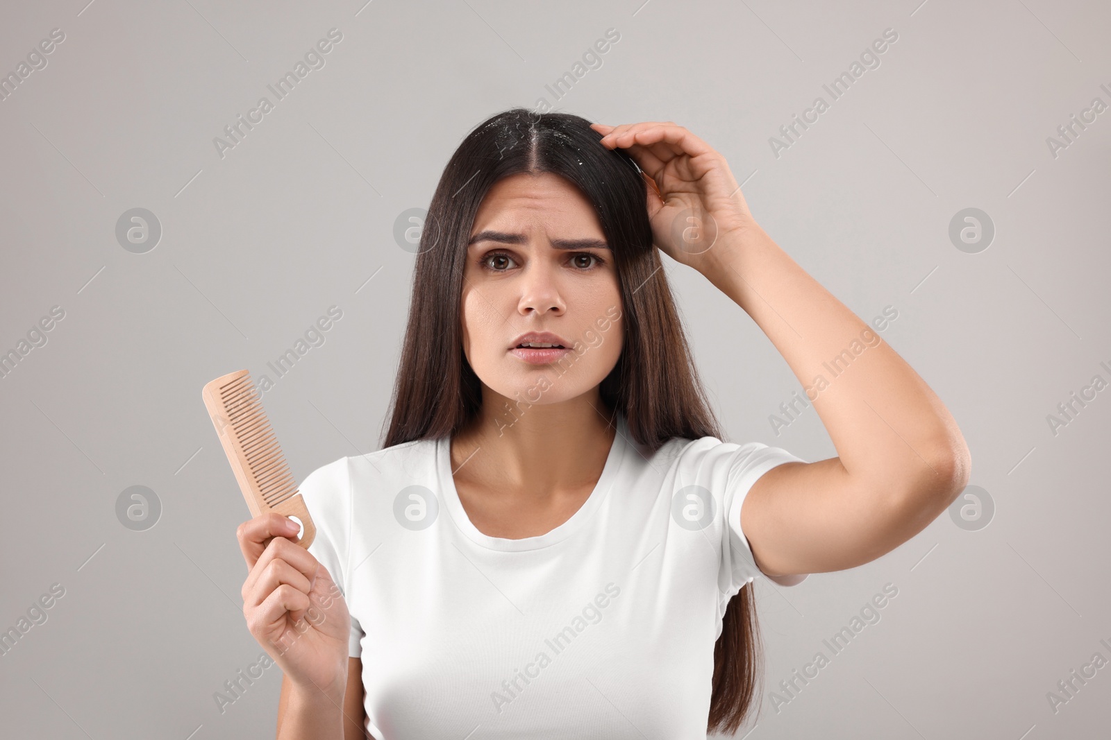 Photo of Emotional woman with comb examining her hair and scalp on grey background. Dandruff problem