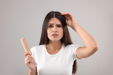 Photo of Emotional woman with comb examining her hair and scalp on grey background. Dandruff problem