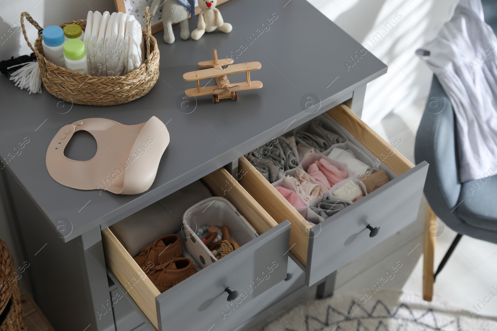 Photo of Open cabinet drawers with clothes and different items in child room