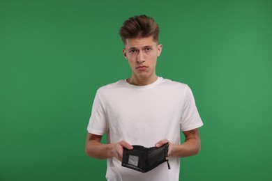 Upset man with empty wallet on green background