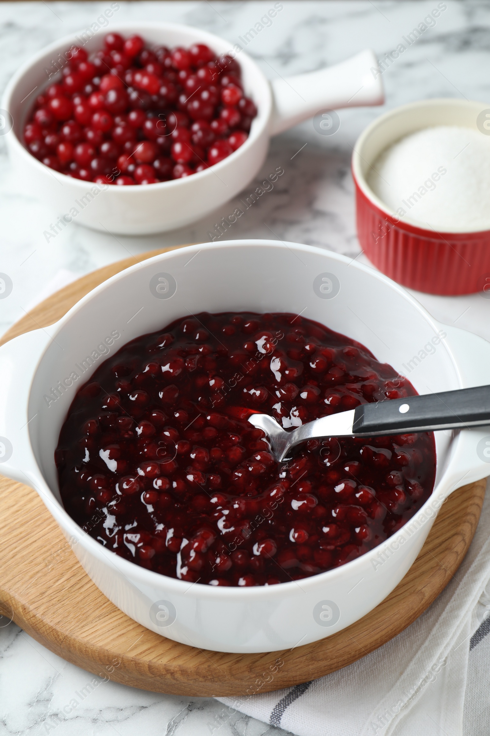 Photo of Fresh cranberry sauce in bowl served on white marble table, closeup