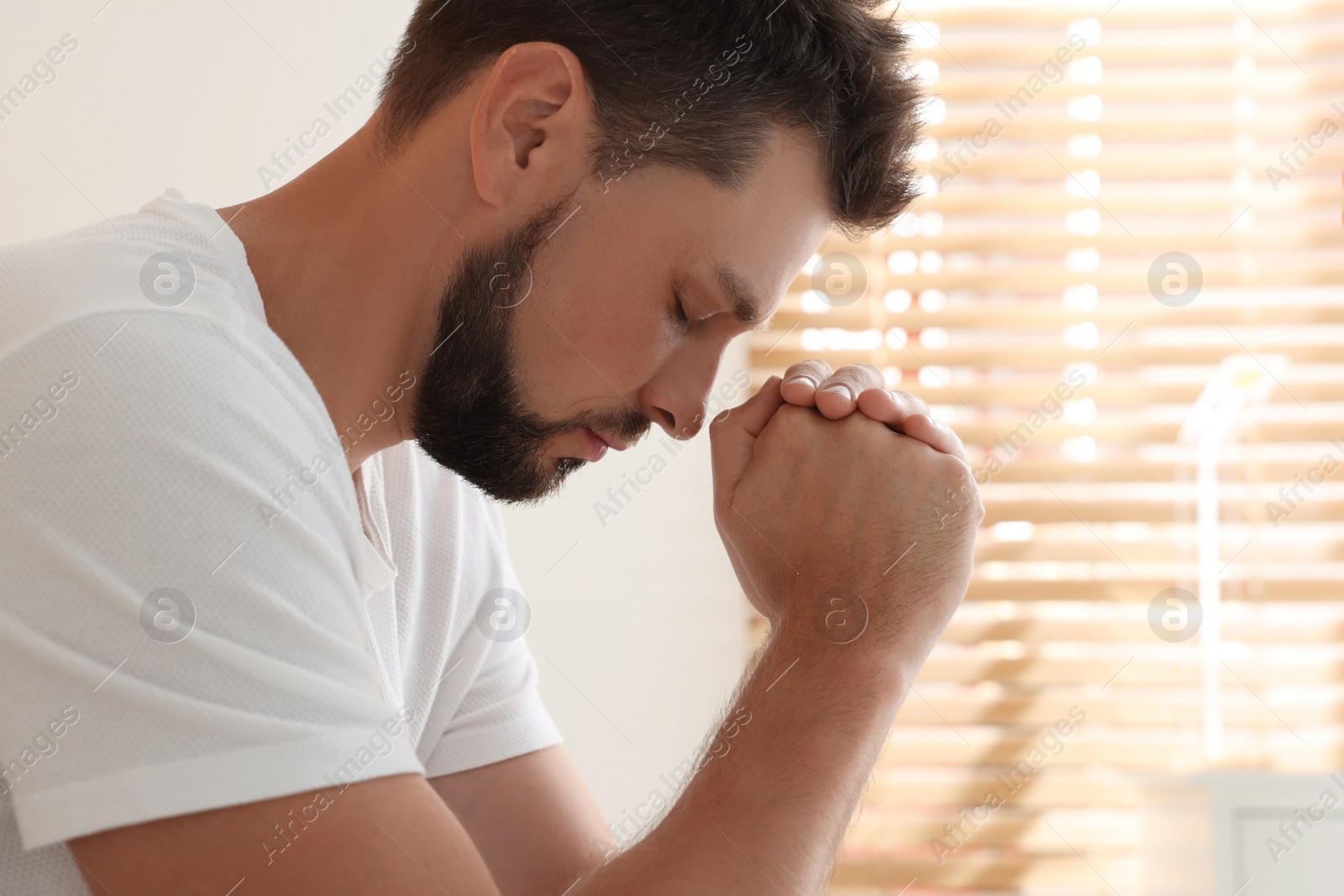 Photo of Religious man with clasped hands praying indoors