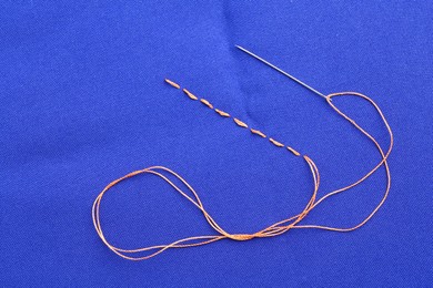 Photo of Sewing needle with thread and stitches on blue cloth, top view
