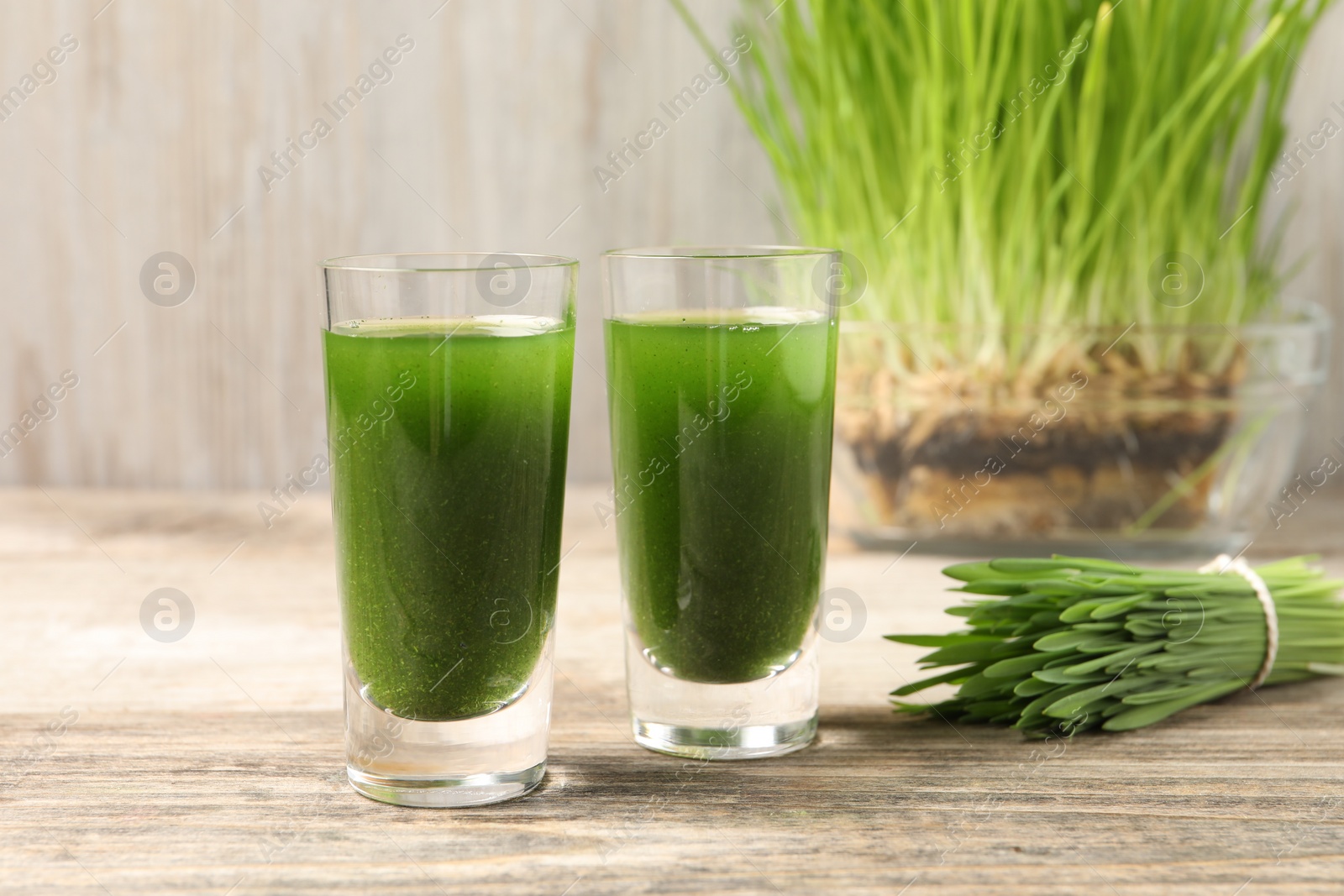 Photo of Wheat grass drink in shot glasses and fresh green sprouts on wooden table, closeup