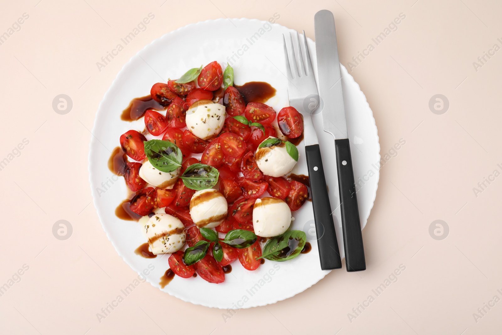 Photo of Tasty salad Caprese with tomatoes, mozzarella balls, basil and cutlery on beige background, top view