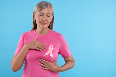 Senior woman with pink ribbon on light blue background, space for text. Breast cancer awareness