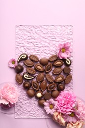 Photo of Heart made with delicious chocolate candies and beautiful flowers on pink background, flat lay
