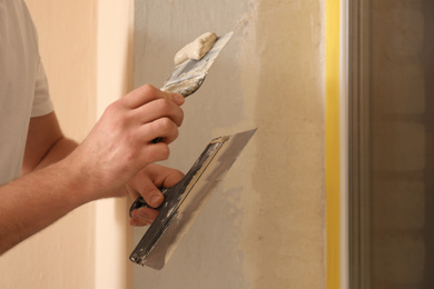 Photo of Man plastering window area with putty knife indoors, closeup. Interior repair