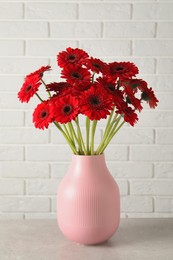 Bouquet of beautiful red gerbera flowers on table near white brick wall