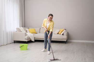 Photo of Young woman cleaning floor with mop in living room