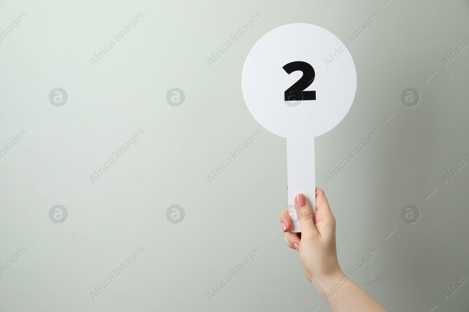 Photo of Woman holding auction paddle with number 2 on light grey background, closeup. Space for text