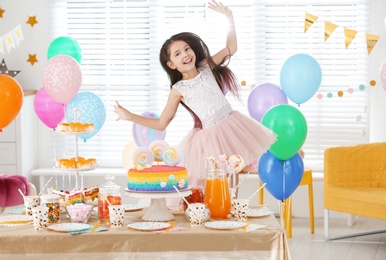 Happy girl at table with treats in room decorated for birthday party