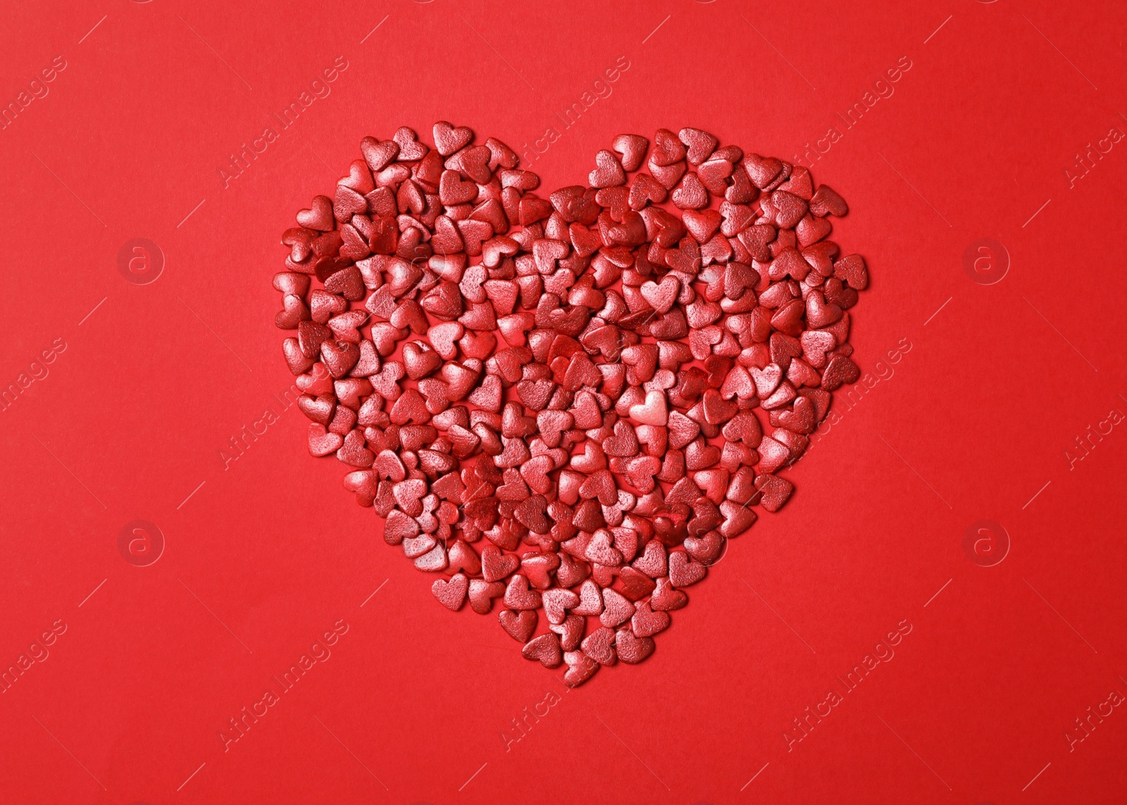 Photo of Heart made of bright sprinkles on red background, flat lay