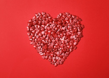 Photo of Heart made of bright sprinkles on red background, flat lay