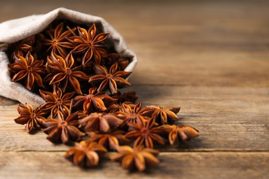 Photo of Overturned bag with aromatic anise stars on wooden table, closeup. Space for text