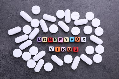 Words Monkeypox Virus made of cubes and pills on grey table, flat lay