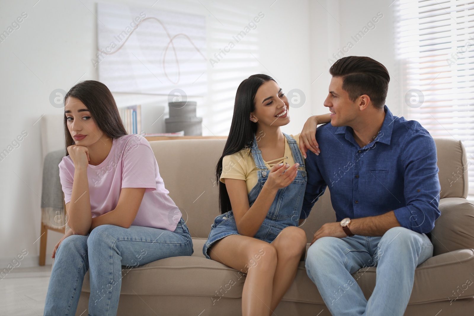 Photo of Unhappy woman feeling jealous while couple spending time together on sofa at home