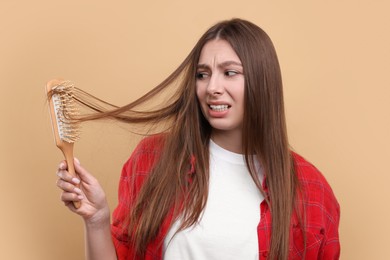 Photo of Emotional woman brushing her hair on beige background. Alopecia problem