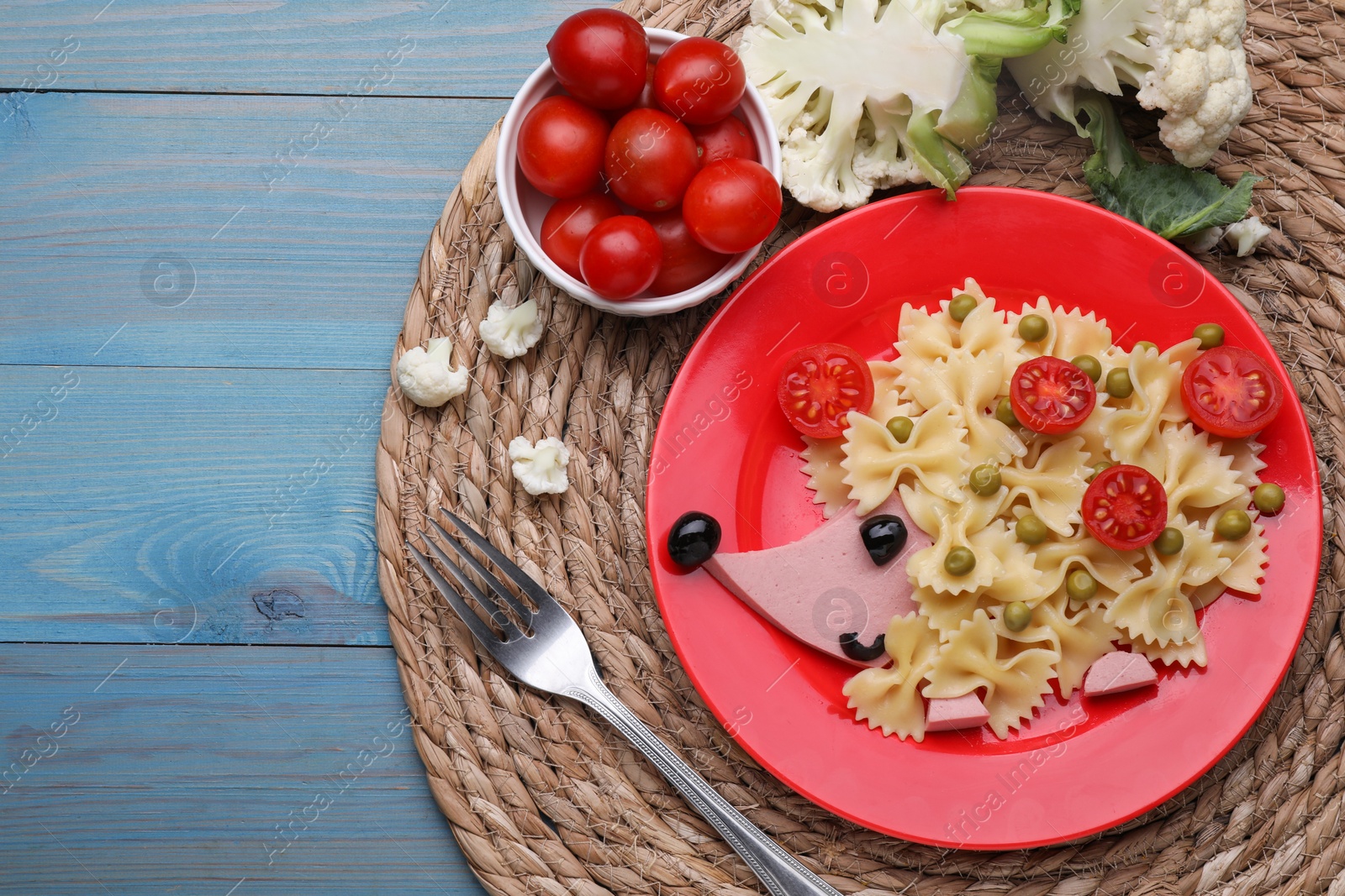 Photo of Creative serving for kids. Plate with cute hedgehog made of delicious pasta, sausages and tomatoes on light blue wooden table, flat lay. Space for text