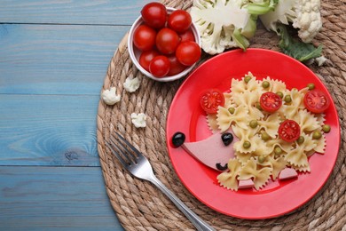 Creative serving for kids. Plate with cute hedgehog made of delicious pasta, sausages and tomatoes on light blue wooden table, flat lay. Space for text