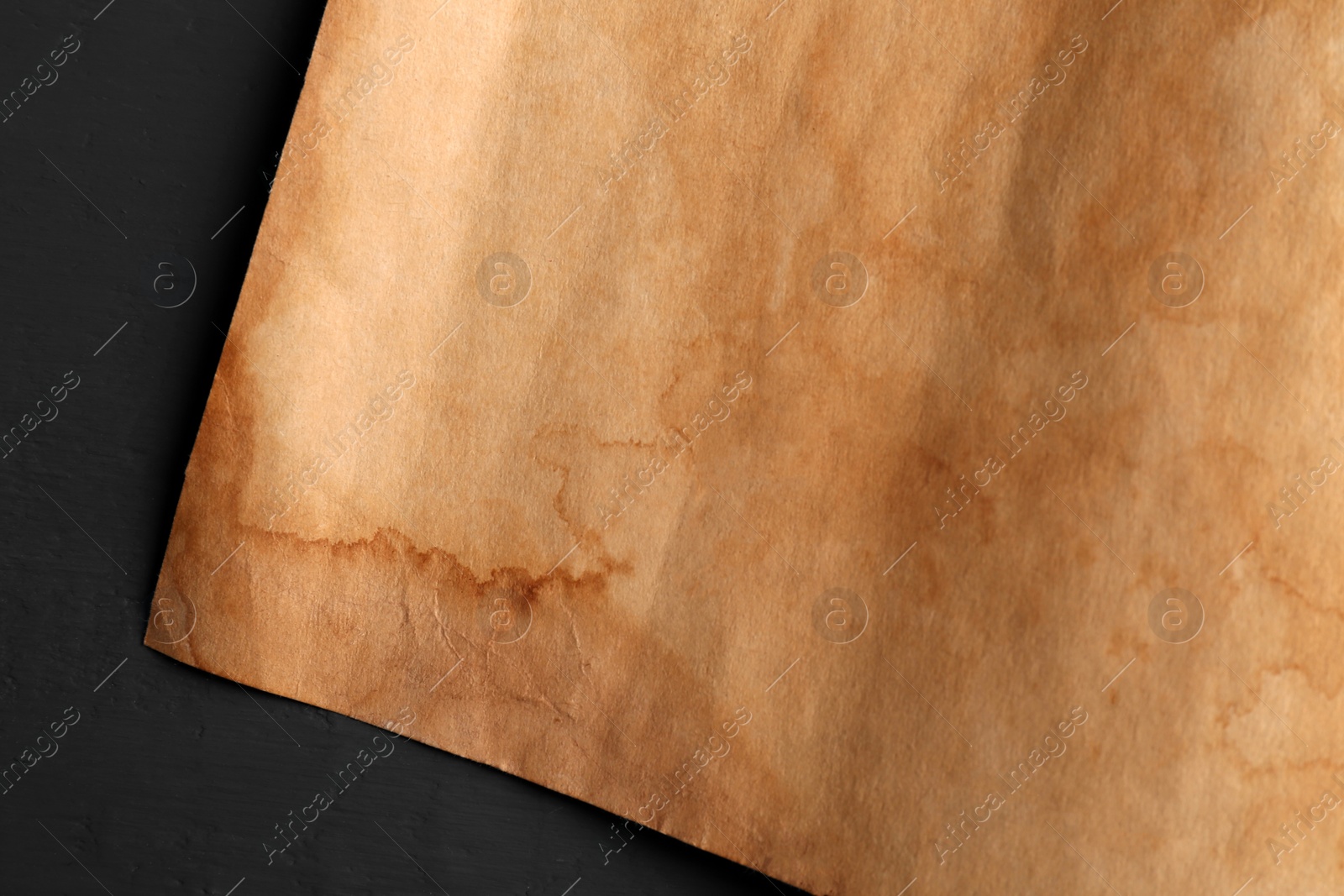 Photo of Sheet of old parchment paper on black wooden table, top view
