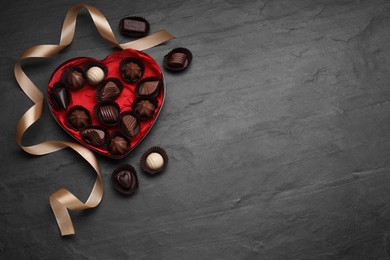 Photo of Heart shaped box with delicious chocolate candies and ribbon on grey table, flat lay. Space for text
