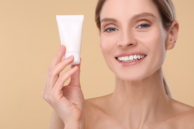 Woman holding tube of foundation on beige background