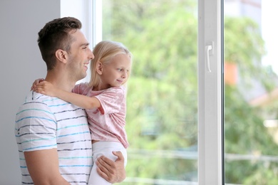 Photo of Young man with cute little girl near window at home
