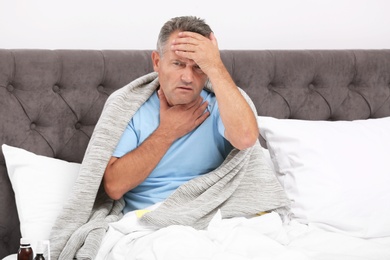 Photo of Man suffering from cough and headache in bed at home