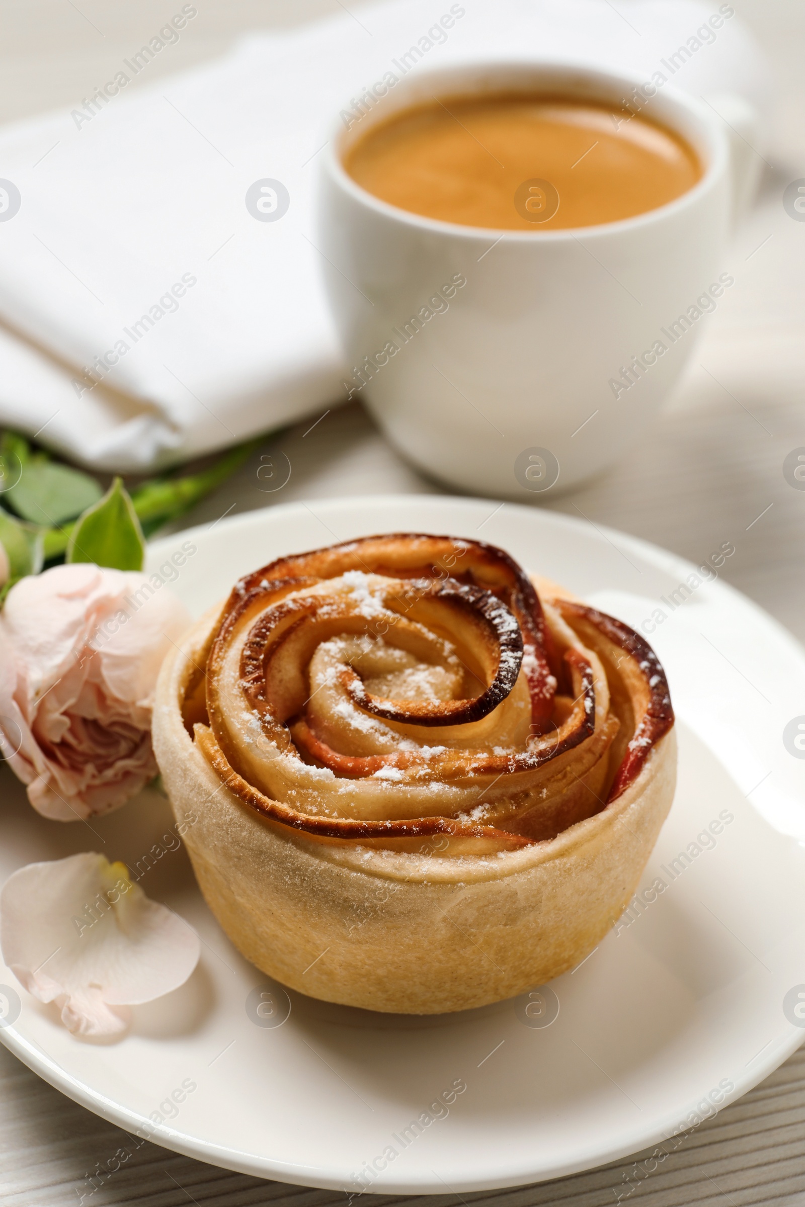 Photo of Freshly baked apple rose, cup of coffee and beautiful flowers on white wooden table