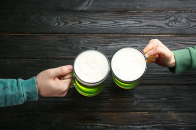 Photo of Man and woman toasting with green beer at black wooden table, top view. St. Patrick's Day celebration