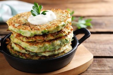 Photo of Delicious zucchini fritters with sour cream on wooden table, closeup