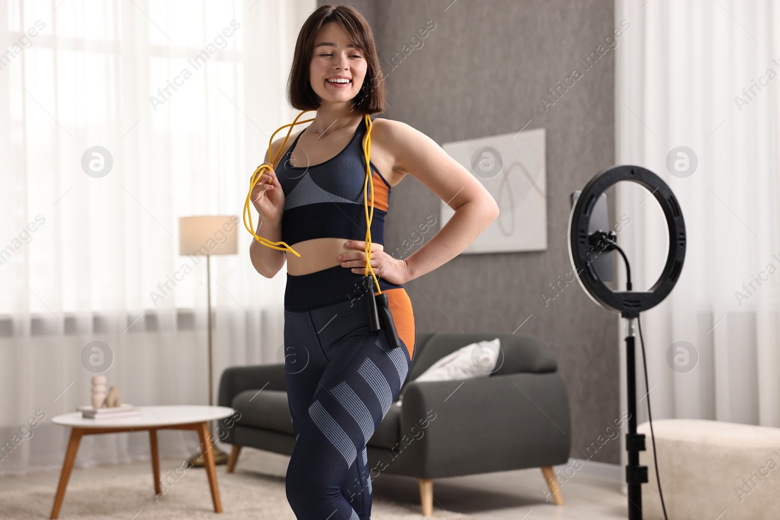 Photo of Happy sports blogger with skipping rope streaming online fitness lesson with smartphone at home