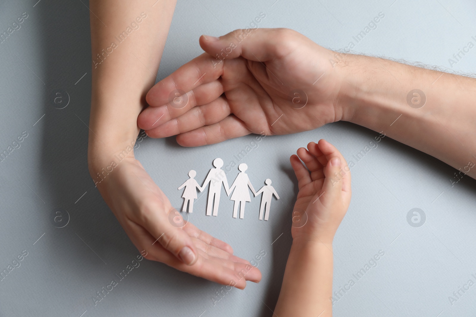 Photo of Parents and child holding paper family figures on gray background, top view