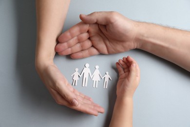 Photo of Parents and child holding paper family figures on gray background, top view