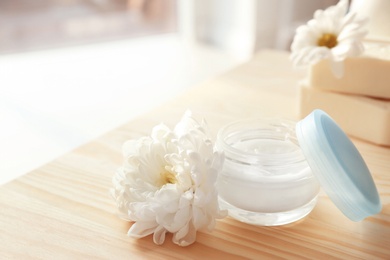 Photo of Jar with body care cream and flower on table