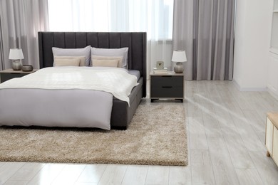 Photo of Stylish bedroom in soft light colors with comfortable bed and bedside tables. Interior design
