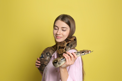 Young woman with boa constrictor on yellow background. Exotic pet