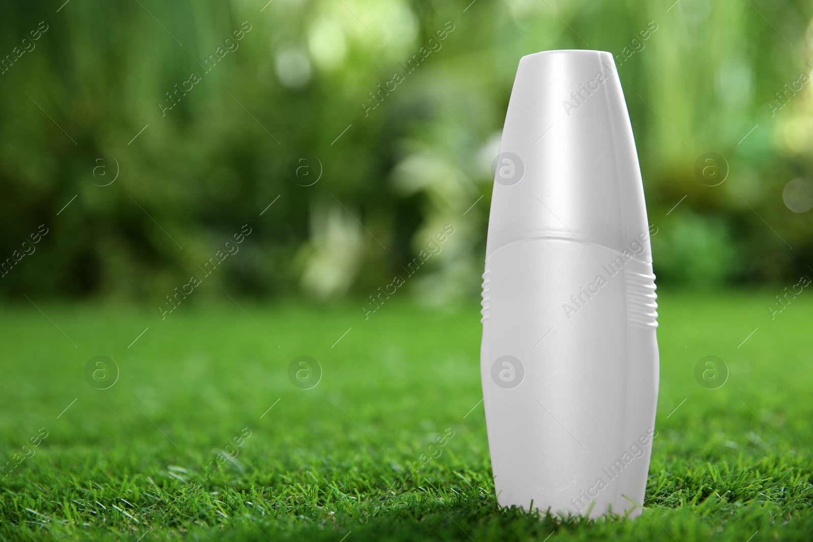 Photo of Bottle of insect repellent spray on green grass. Space for text