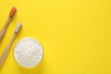 Photo of Bowl of tooth powder and brushes on yellow background, flat lay. Space for text