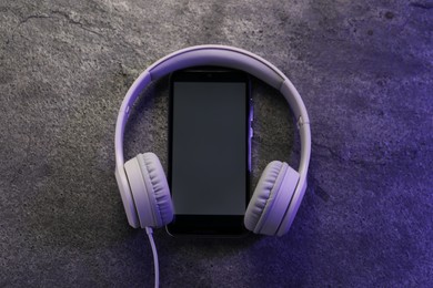 Photo of Smartphone with blank screen and headphones on grey textured background, top view with space for text. Sound equipment
