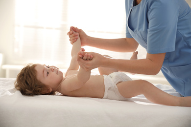 Orthopedist examining little baby on bed indoors