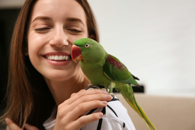 Photo of Young woman with cute Alexandrine parakeet indoors
