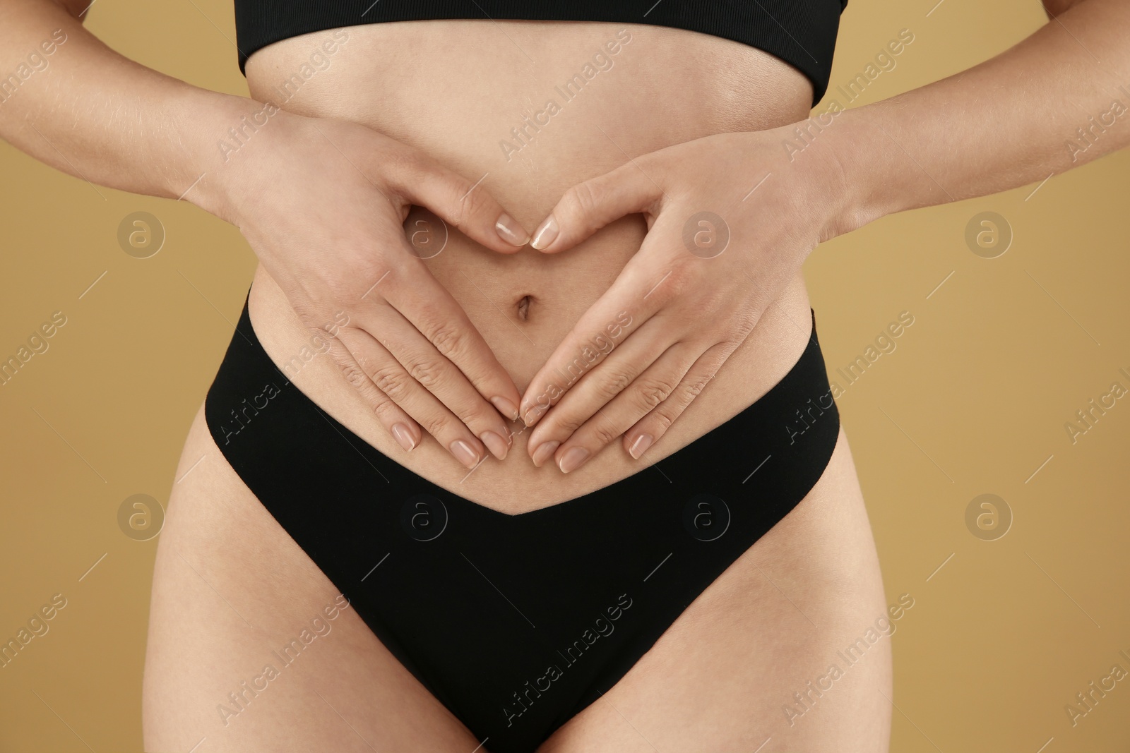 Photo of Gynecology. Woman in underwear making heart with her hands on beige background, closeup