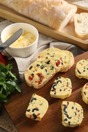 Photo of Tasty butter with olives, chili pepper, parsley and bread on wooden table