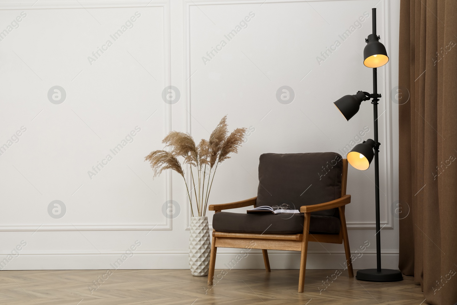 Photo of Stylish armchair with book, floor lamp and spikes near white wall indoors, space for text. Interior design