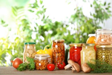 Photo of Glass jars of different pickled vegetables on wooden table