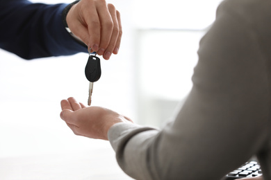 Photo of Salesman giving key to customer on light background, closeup. Buying new car